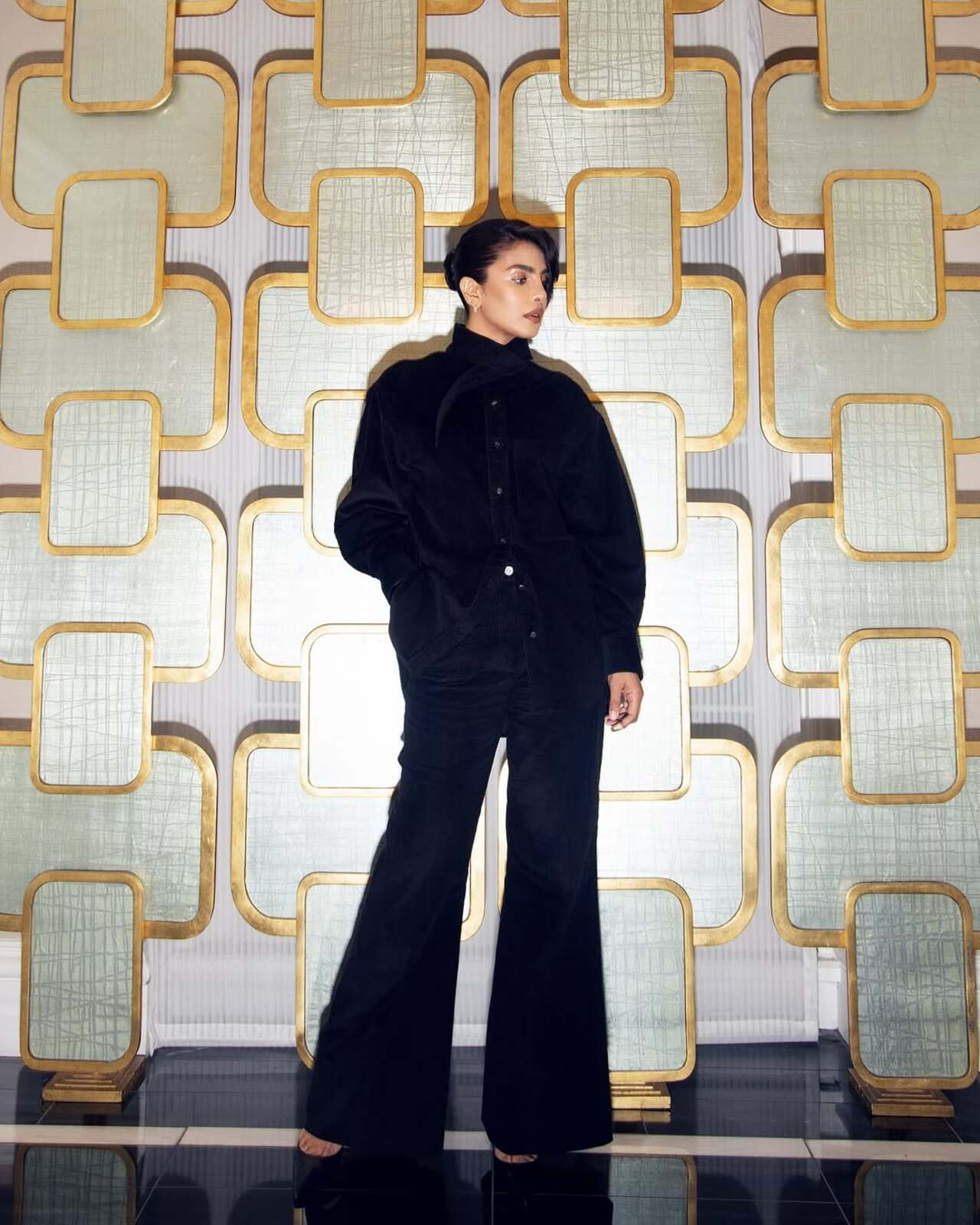 A lesson in power dressing with a luxurious twist: Priyanka commands attention in a plush black velvet coordinated set featuring wide-leg trousers and a softly structured shirt. The monochrome palette and minimalist styling emphasize clean lines, while her slicked-back hair and muted lips elevate the ensemble to contemporary chic